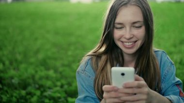 Çimenlerin üzerinde oturan genç güzel kız ve telefonda gösterir