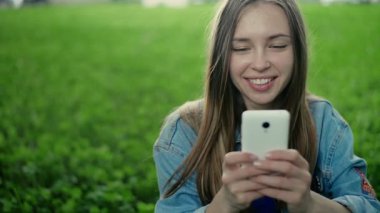 Çimenlerin üzerinde oturan genç güzel kız ve telefonda gösterir