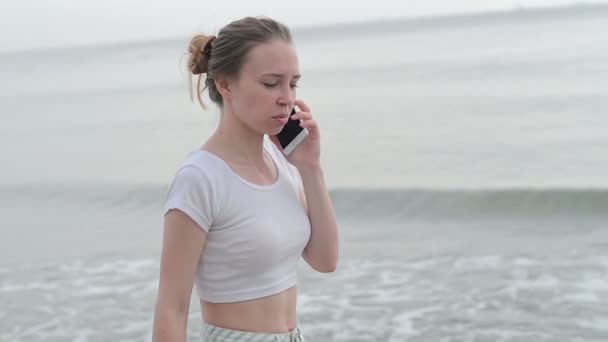 Ung kvinna med mobiltelefon på en strand — Stockvideo