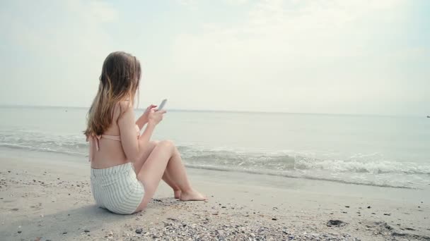 Молодая женщина с сотовым телефоном на пляже, стреляла в куклу — стоковое видео