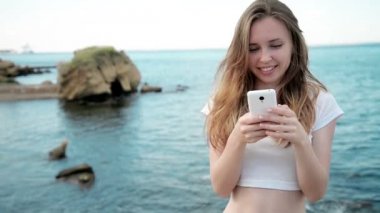 Holding ve gün batımı Hawaii plajda akıllı telefon bakarak karışık yarış oldukça gülümseyen genç kadın