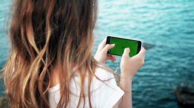 Genç kız Holding Smartphone ile akşam saat denizde Yeşil perde