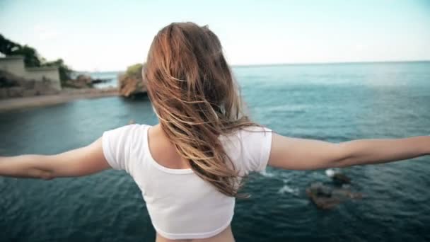 The young woman raised her hand up to the sun, against the sea, rocks and sky with clouds — Stock Video