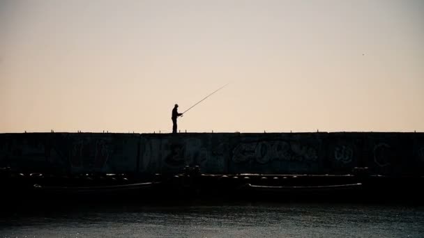 Muž, rybaření ze zdi vlnolamů průmyslové zázemí při západu slunce — Stock video