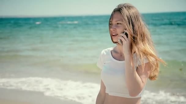 Hermosa mujer joven en bikini hablando de teléfono inteligente en la playa del mar. Soleado verano junto al mar — Vídeos de Stock