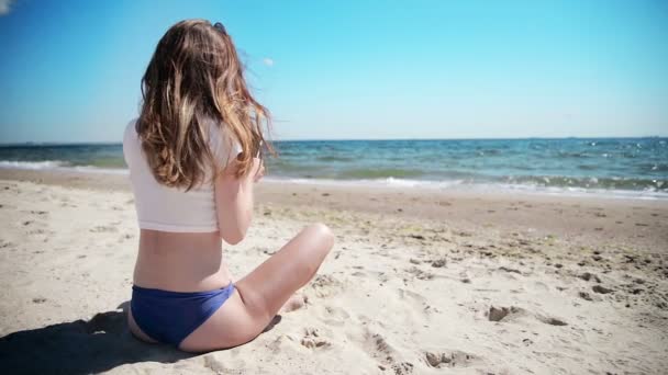 Flicka med mobiltelefon sitter på sand nära havet och blå himmel. Första kärlek. — Stockvideo