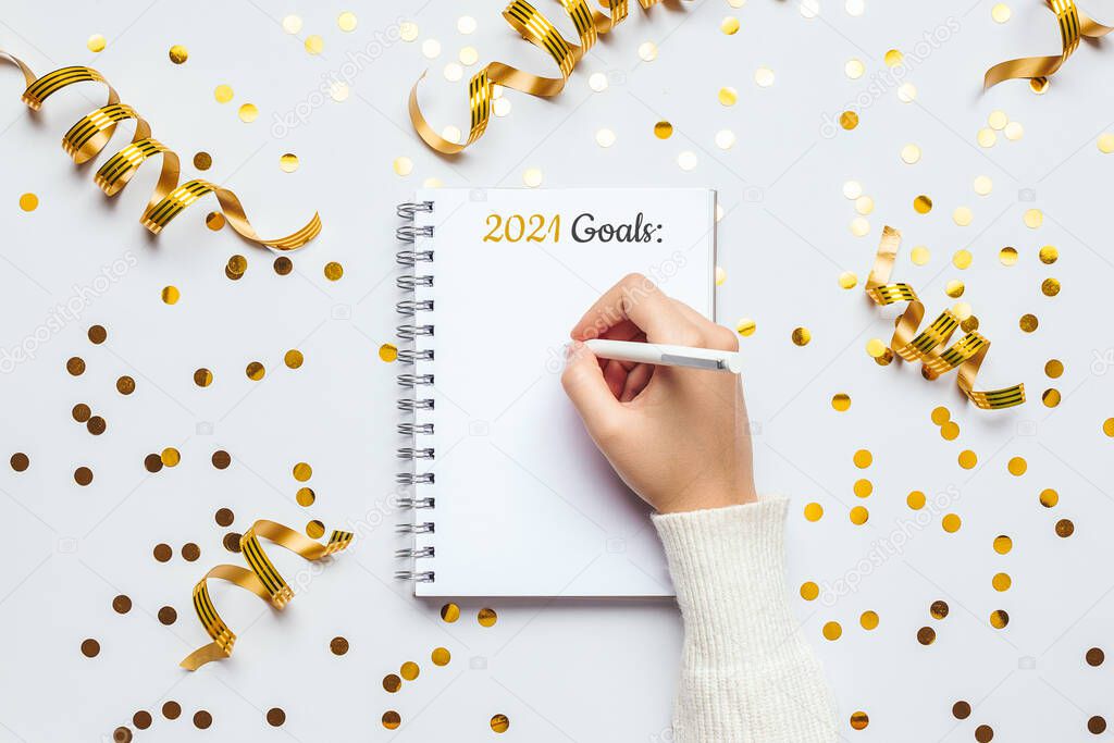Stock photo of 2021 new year resolutions notebook with festive decorations on a white table, flat lay style. Planning concept