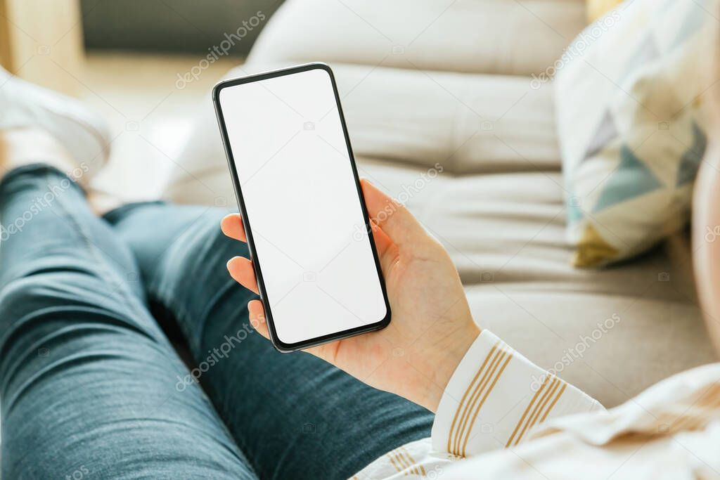 Mockup of a phone held by a woman's hand who is sitting on the couch. White screen