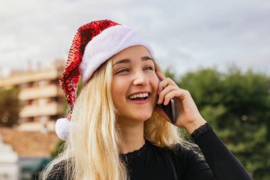 Yılbaşı için akıllı telefondan arayan genç ve mutlu bir sarışın kadının stok fotoğrafı. Konuşuyor ve gülümsüyor. Mutlu Xmas, insanlar ve teknoloji konsepti