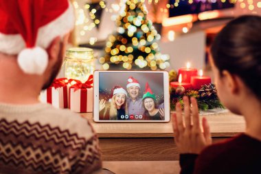 Genç bir çiftin Noel 'de aileleriyle görüntülü konuşma yaparken çekilmiş fotoğrafı. Aile kavramı, koronavirüs yüzünden Noel boyunca karantinada. Xmas hala rahat bir odada tabletle yaşıyor.
