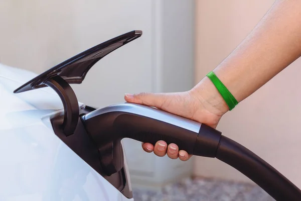 Woman's hand plugging in the charger to a electric vehicle or EV car at a charging station. The future of the Automobile and Eco-friendly alternative energy concept