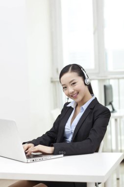 Dizüstü bilgisayar kullanan ve kulaklık takan genç bir kadın.