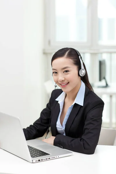 Młoda kobieta używająca laptopa i nosząca słuchawki — Zdjęcie stockowe