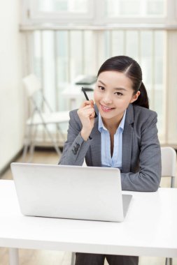 Genç bir kadın dizüstü bilgisayarın önünde oturuyor.