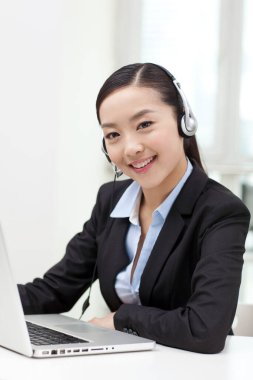 Dizüstü bilgisayar kullanan ve kulaklık takan genç bir kadın.