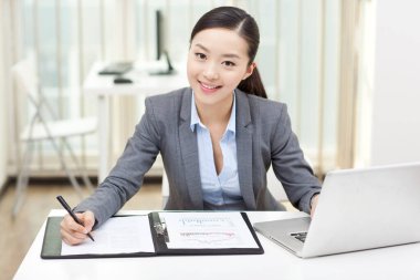 Genç bir kadın dizüstü bilgisayarın önünde oturuyor.