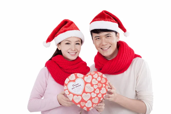 Retrato de jovem casal vestindo chapéus de Papai Noel, segurando presente — Fotografia de Stock