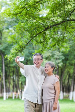 Mutlu yaşlı çift parkta cep telefonuyla selfie çekiyor.
