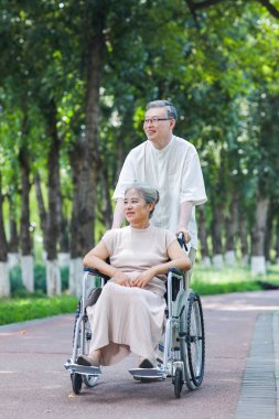 Yaşlı adam karısını tekerlekli sandalyeye itiyor.