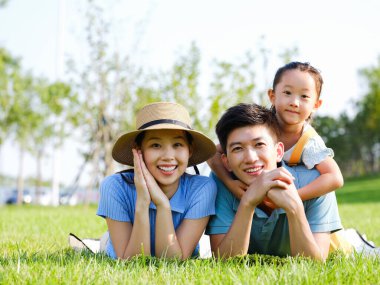 Üç kişilik mutlu bir aile çimlerin üzerinde yatıyor.