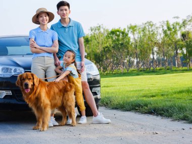 Üç kişilik mutlu bir aile ve arabanın önünde evcil bir köpek.