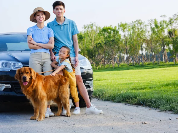 Happy family of three and pet dog in front of car