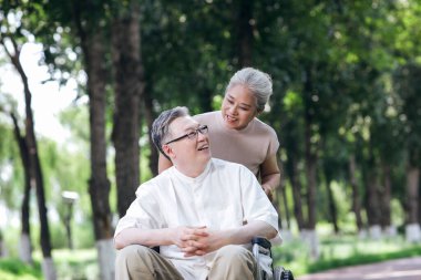 Yaşlı adam karısını tekerlekli sandalyeye itiyor.
