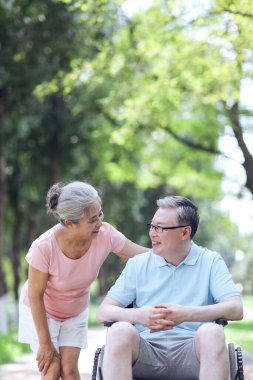 Yaşlı adam karısını tekerlekli sandalyeye itiyor.