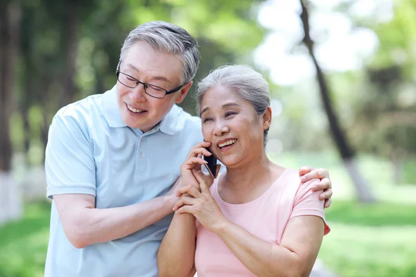 幸せな老夫婦は屋外で呼び出しを行うために携帯電話を使用 — ストック写真