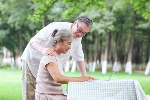 Feliz pareja de edad utilizar el ordenador para navegar por Internet al aire libre —  Fotos de Stock