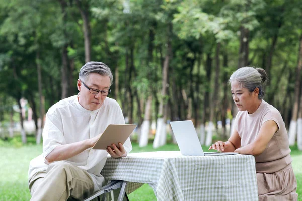 Happy old couple use computer to surf the Internet outdoors