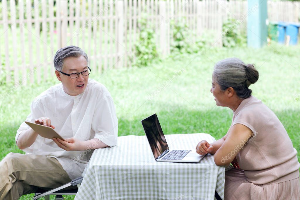 Happy old couple use computer to surf the Internet outdoors