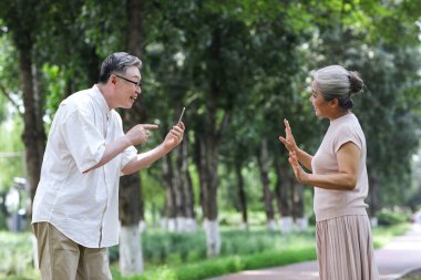 Mutlu yaşlı çift parkta cep telefonuyla fotoğraf çekiyor.