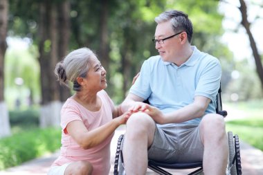 Yaşlı adam karısını tekerlekli sandalyeye itiyor.