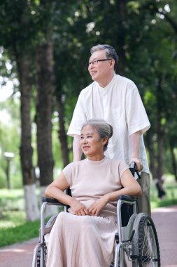 Yaşlı adam karısını tekerlekli sandalyeye itiyor.
