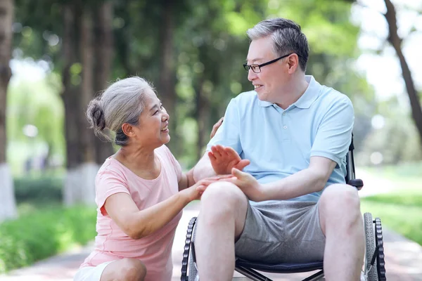 Yaşlı adam karısını tekerlekli sandalyeye itiyor.