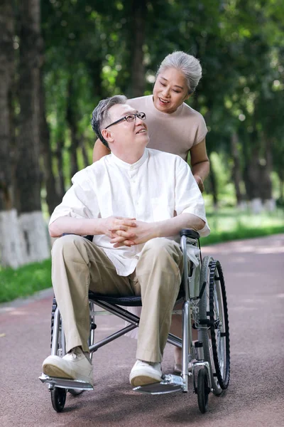 O velho empurra sua esposa em uma cadeira de rodas — Fotografia de Stock