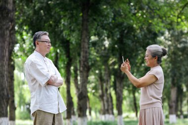 Mutlu yaşlı çift parkta cep telefonuyla fotoğraf çekiyor.