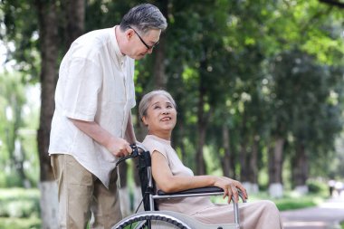 Yaşlı adam karısını tekerlekli sandalyeye itiyor.