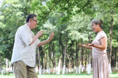 Mutlu yaşlı çift parkta cep telefonuyla fotoğraf çekiyor.