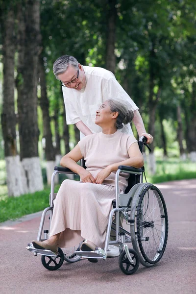 O velho empurra sua esposa em uma cadeira de rodas — Fotografia de Stock