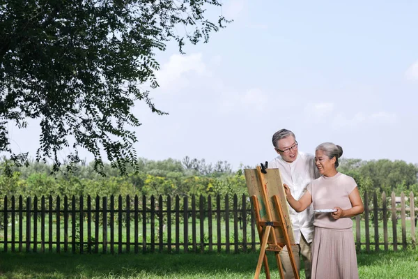 Happy old couple painting in the park