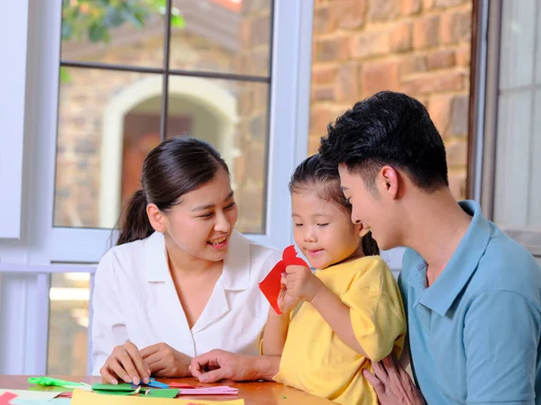 En lycklig familj på tre som gör pappersurklipp i vardagsrummet — Stockfoto
