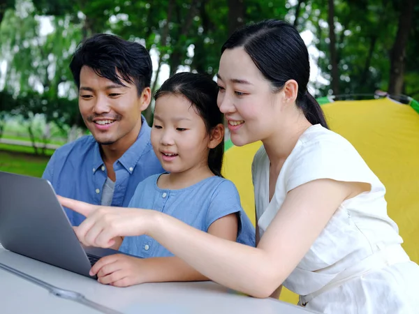 Familia feliz de tres utilizan la computadora para navegar por Internet al aire libre — Foto de Stock