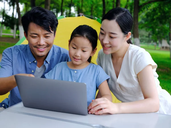 Família feliz de três usar computador para navegar na Internet ao ar livre — Fotografia de Stock