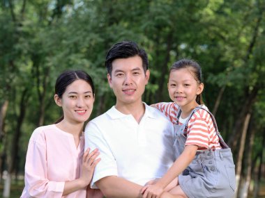 Üç kişilik mutlu bir aile parkta oynuyor.