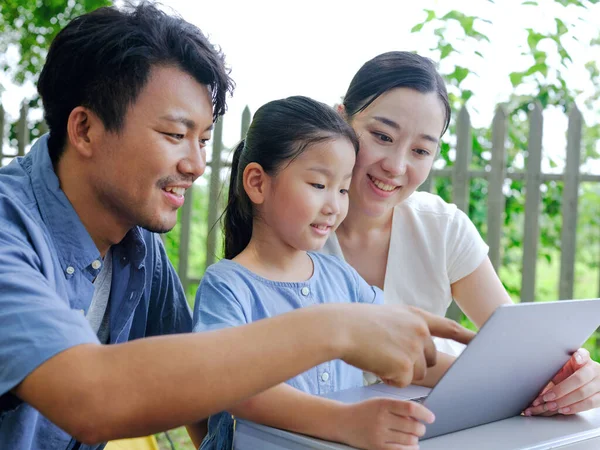 Família feliz de três usar computador para navegar na Internet ao ar livre — Fotografia de Stock