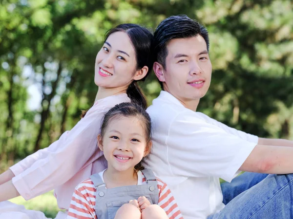 Щаслива сім'я з трьох сидить на парковій траві — стокове фото