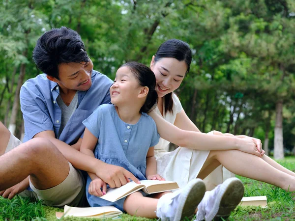 Una famiglia felice di tre persone sta leggendo all'aperto — Foto Stock