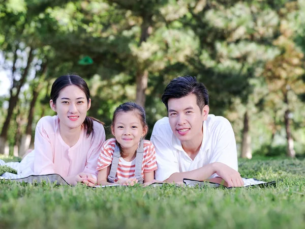 Familia feliz de tres en el césped del parque —  Fotos de Stock